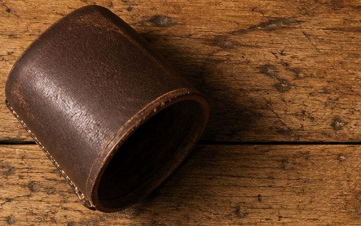 Mesa de madeira gasta com marcas de copo, um copo de couro de dados deitado no canto e a palavra SERVIDO! gravada a fogo na madeira.